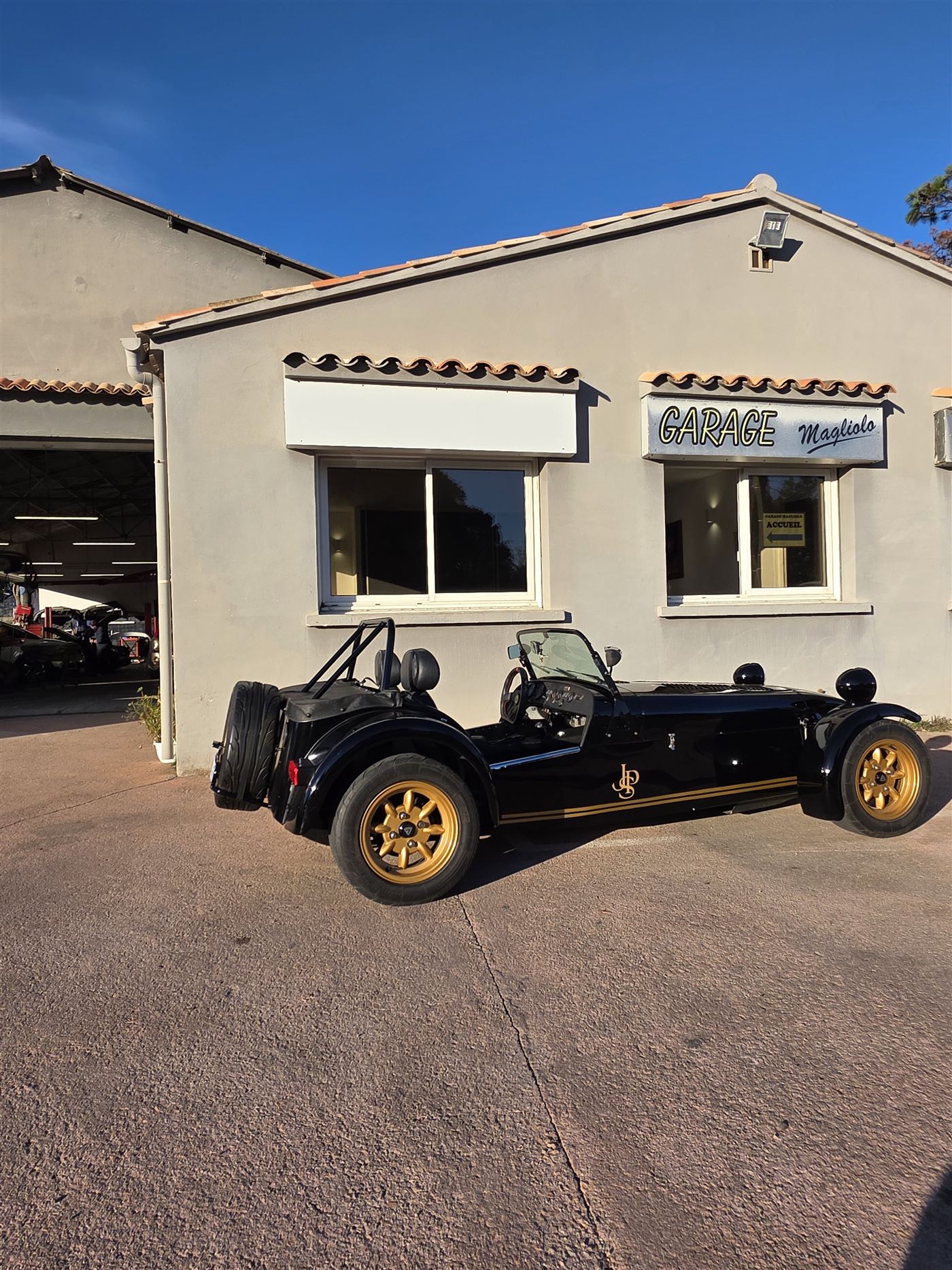 Caterham noire et or devant le Garage Magliolo